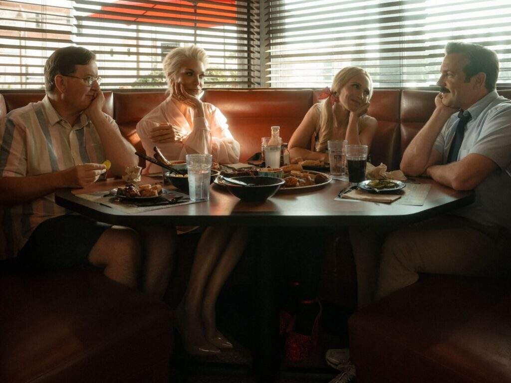 From left to right: Higgins (Jeremy Swift), Rebecca (Hannah Waddingham), Keeley (Juno Temple), and Ted (Jason Sudeikis) are bonding in a Kansas City barbecue restaurant.