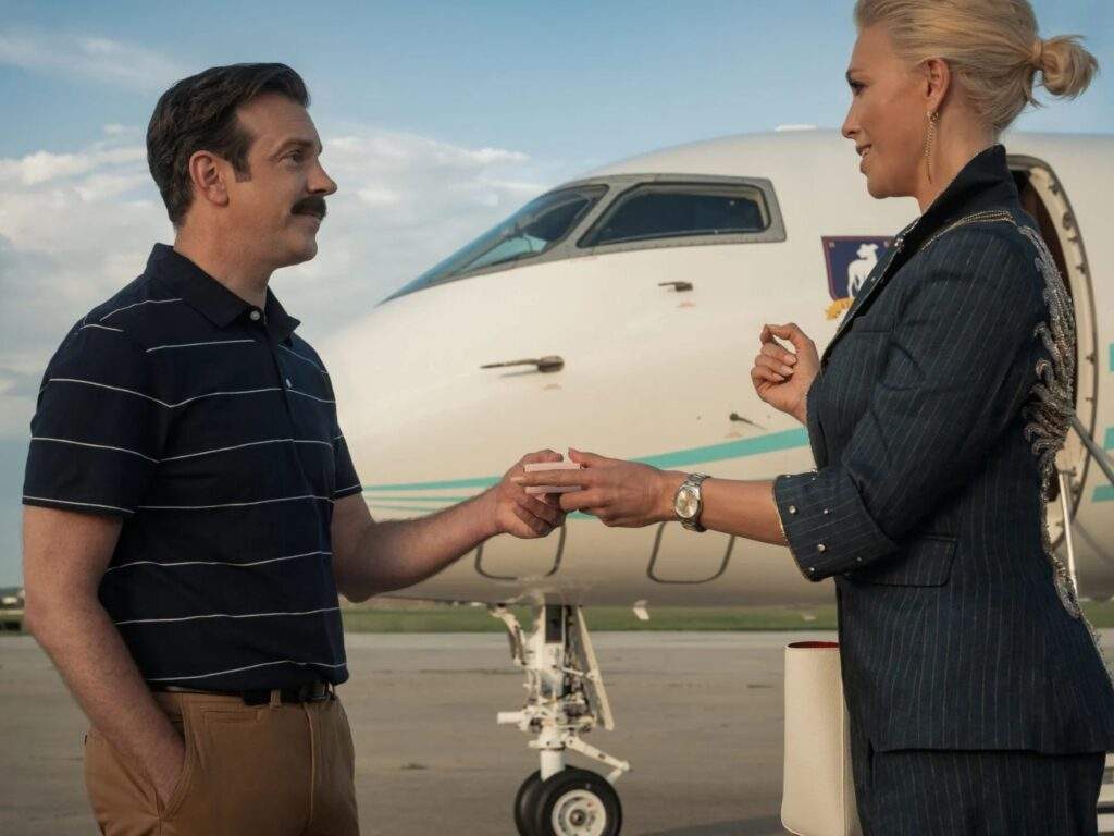 Ted Lasso (Jason Sudeikis) and Rebecca Welton (Hannah Waddingham) say goodbye to each other at the tarmac before the latter leaves Kansas City, with her private jet in the background. Rebecca hands Ted a parting gift, which is later revealed to be an English tea bag.