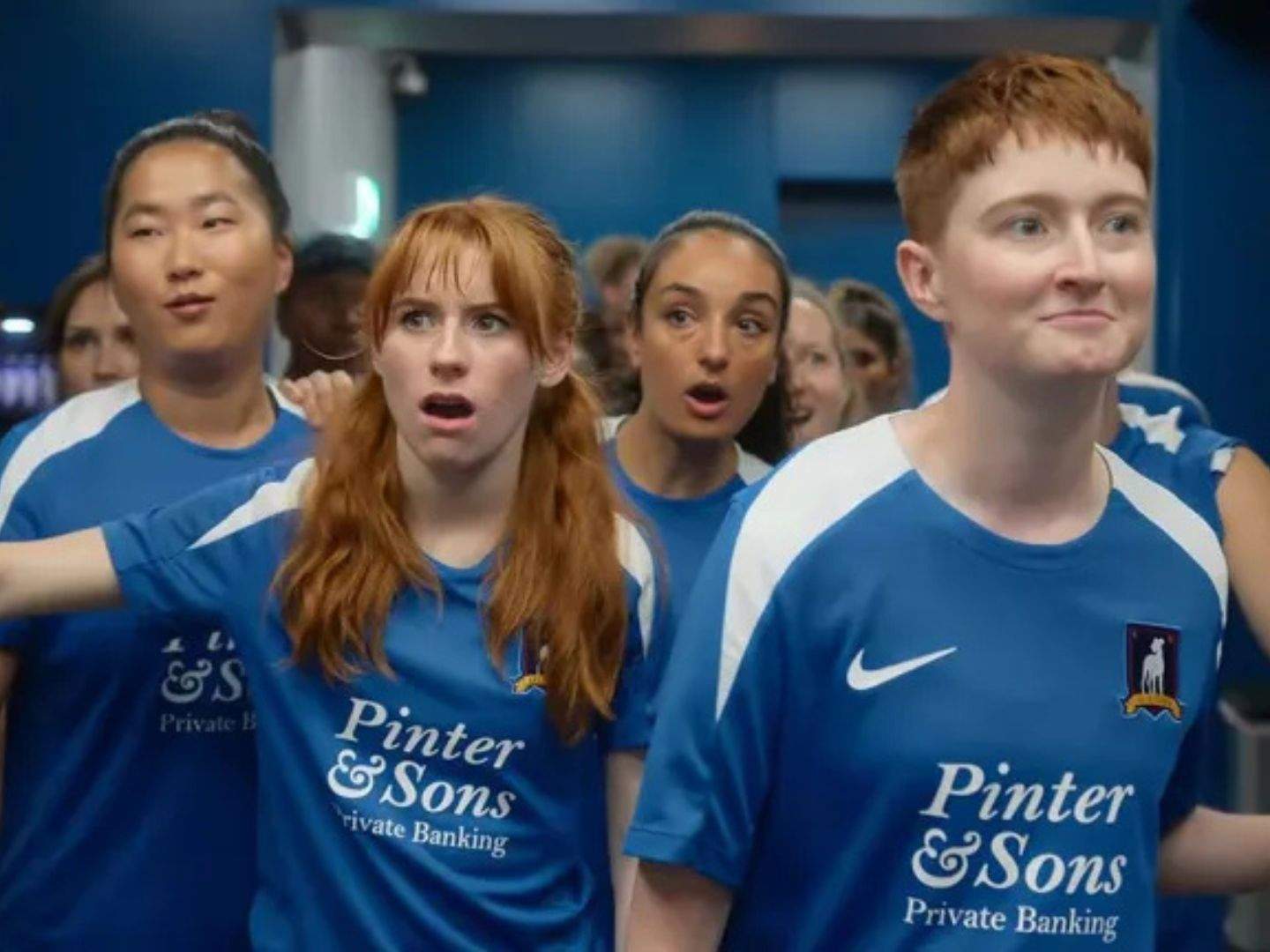 Ted Lasso's women football team, wearing their training kits, enters their new locker room for the first time, much to their awe.