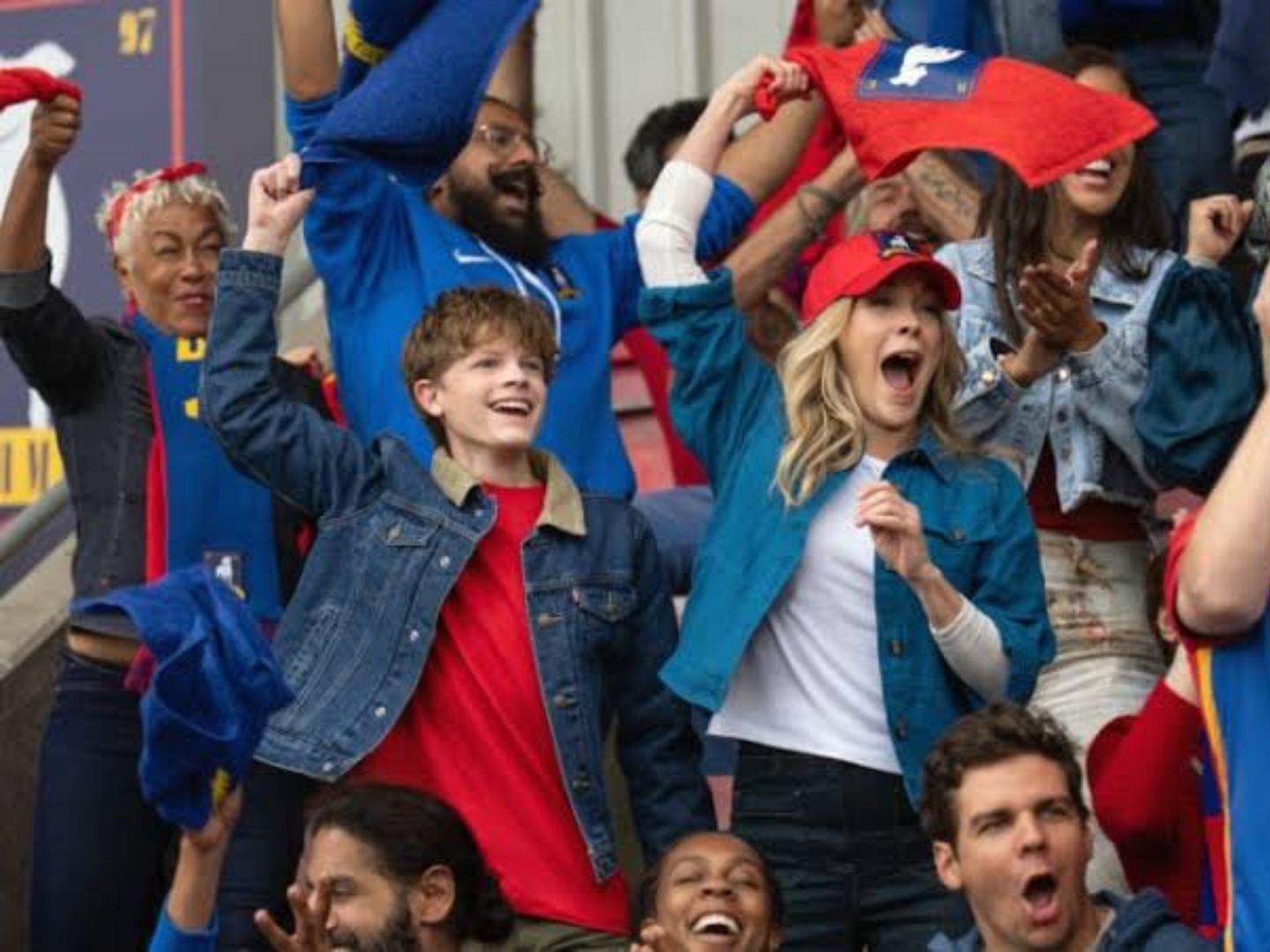 Ted Lasso's son Henry (Grant Feely) and Michelle (Andrea Anders) celebrate Richmond's victory from the stands along with other fans.