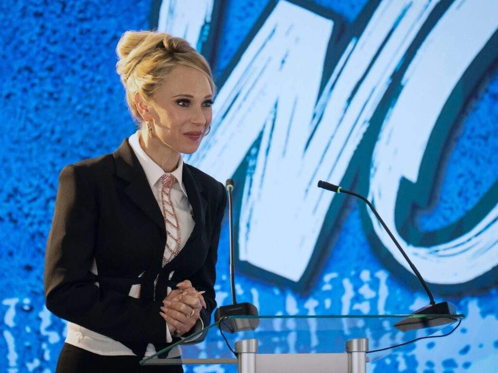 Keeley Jones (Juno Temple), dressed wearing a necktie and a blazer, speaks behind a podium at the AFC Richmond stakeholders' meeting.