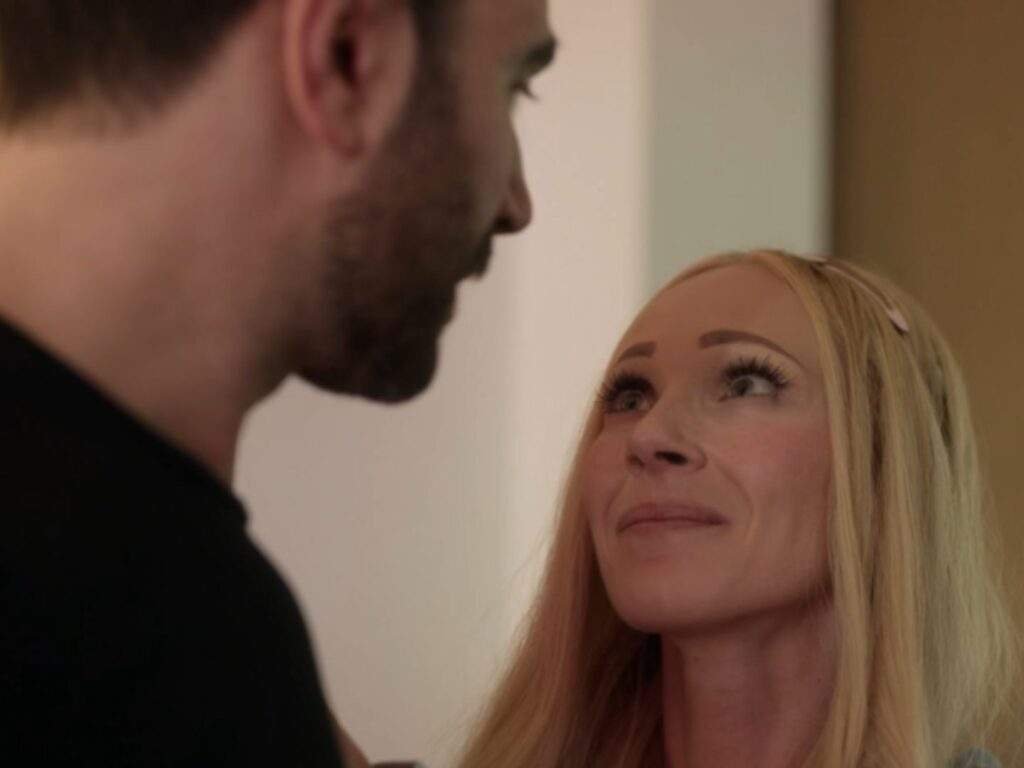 Roy (Brett Goldstein) and Keeley (Juno Temple) share a quiet, emotional moment as Keeley smiles warmly up at Roy while standing close together indoors. Ted Lasso season 4