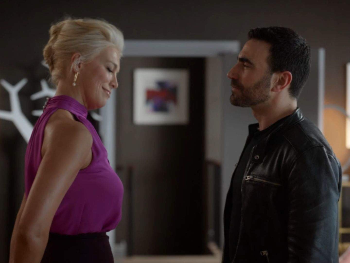 Rebecca Welton (Hannah Waddingham) and Roy Kent (Brett Goldstein) stand face to face in Rebecca's office, sharing a quiet, emotional moment as they smile gently at one another.