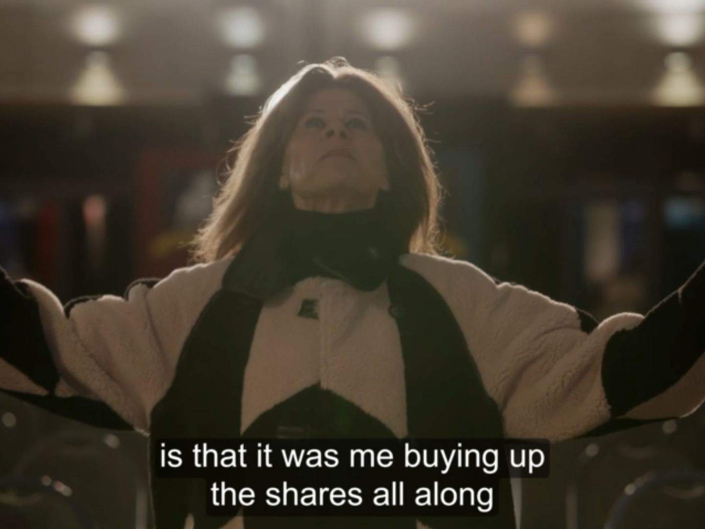 Zelda Southport (Tracey Ullman) stands alone with her arms outstretched beneath bright stadium lights, looking upward in a triumphant moment after revealing her plan.