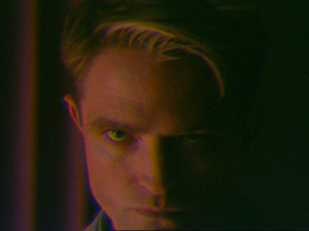 Robert Pattinson as Chris Hansen in Primetime (2026), staring intensely ahead with a stern expression as dim green and reddish lighting partially obscures his face. Primetime