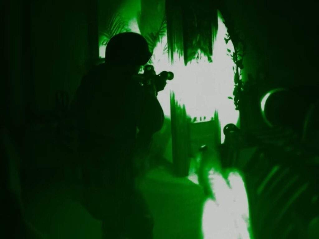 SWAT officers move through a dark, narrow passage illuminated by eerie green light, with one officer aiming a rifle toward a brightly lit opening surrounded by hanging vegetation. Primetime